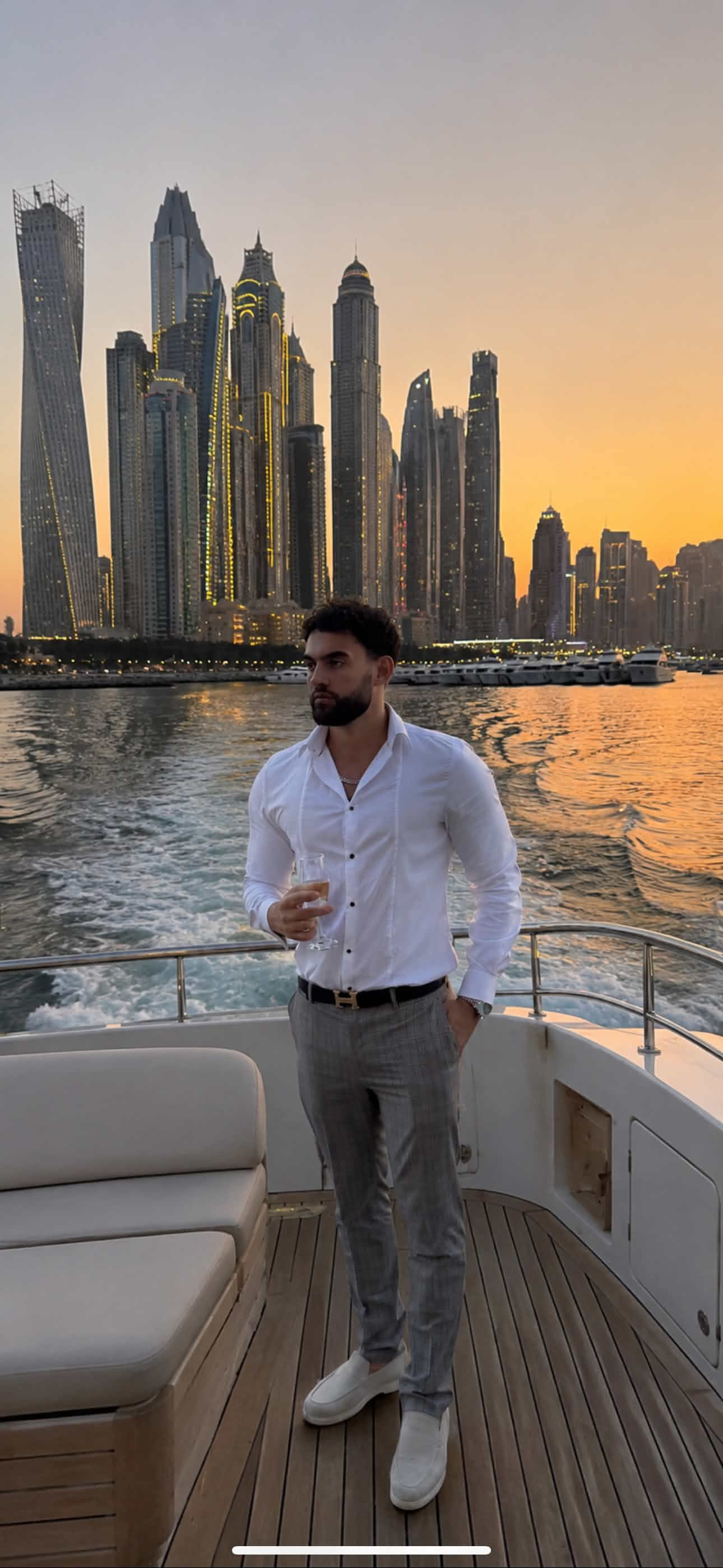 Founder standing aboard a yacht with the Dubai skyline at sunset behind him